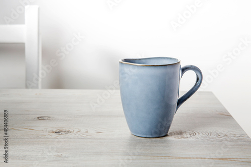 A blue ceramic cup on a beige table against a white wall. Place for text. Copy space