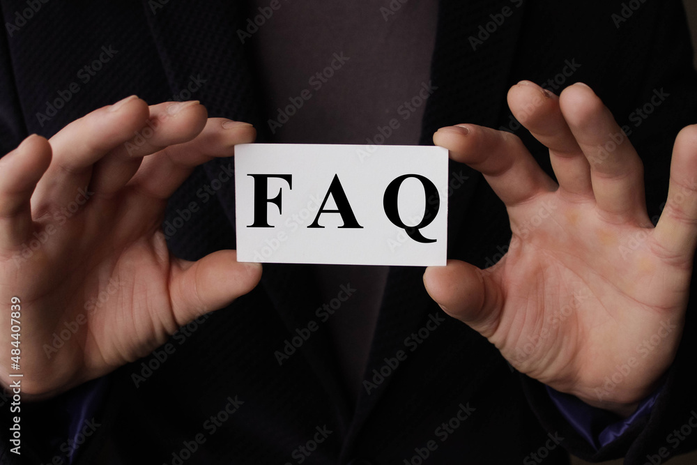 a man wearing a suit sitting in a desk holding a signboard with the word FAQ, Frequently Asked Questions, written in it a man wearing a suit sitting in a desk holding a signboard with the word FAQ, Frequently Asked Questions, written in it