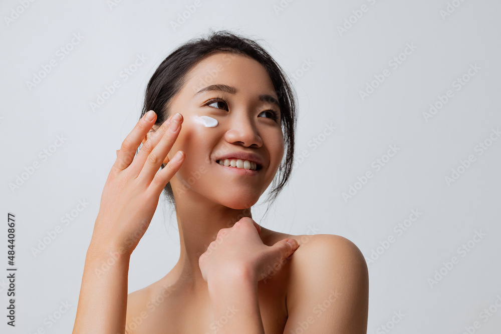 Cropped portrait of young smiling woman doing skincare routine, moisturizing face with special cream Cropped portrait of young smiling woman doing skincare routine, moisturizing face with special cream