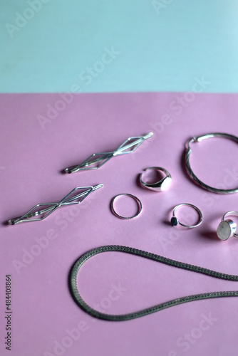 Arrangement of various silver jewelry accessories on pink background. Selective focus.