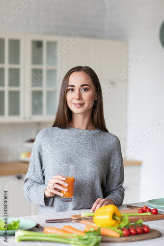 Portrait of a beautiful healthy woman looking at the camera with orange juice in the kitchen while preparing a vegetarian breakfast. Diet