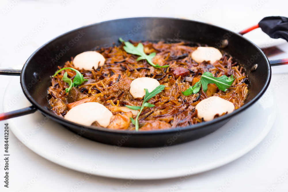 Fideua, served with sauce and arugula. Spanish cuisine.