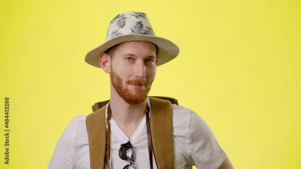 Portrait Of Young Smiling Man With Tourist Backpack, Hat And Camera Standing, Crosses His Arms And Look At Camera On The Yellow Background. The Tourist Goes On Vacation, Traveling Concept People Portrait Of Young Smiling Man With Tourist Backpack, Hat And Camera Standing, Crosses His Arms And Look At Camera On The Yellow Background. The Tourist Goes On Vacation, Traveling Concept People