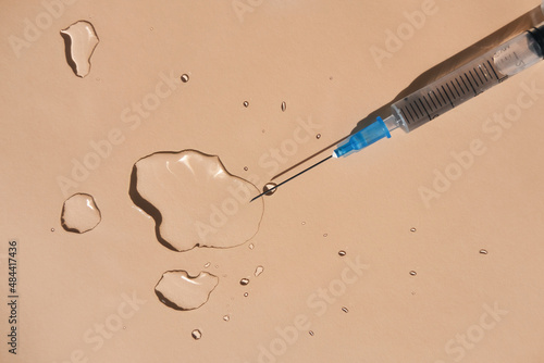 Drops of a transparent liquid and a sterile medical syringe on a beige background. Flat lay, place for text.