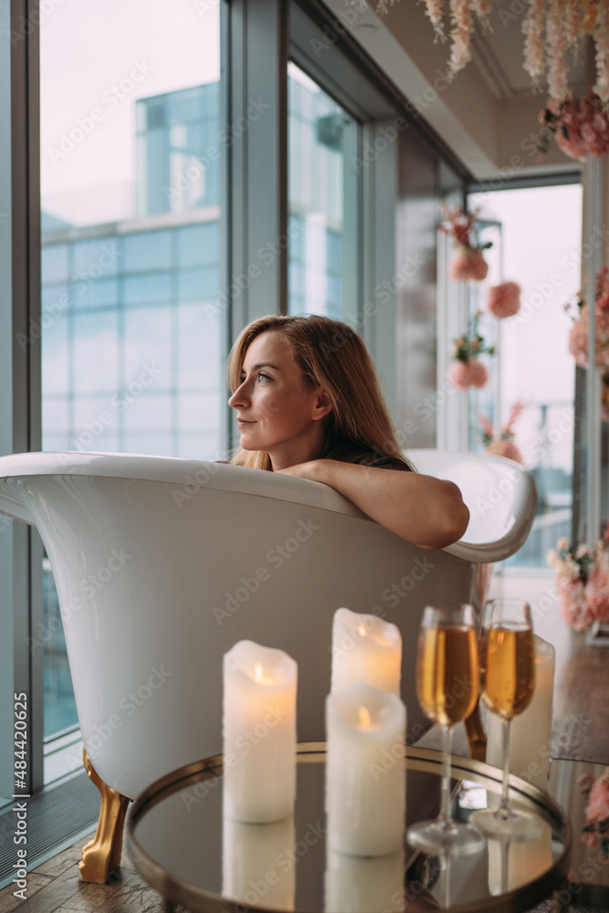 A girl at the window in an empty bathtub with a beautiful view of tall glass buildings A girl at the window in an empty bathtub with a beautiful view of tall glass buildings