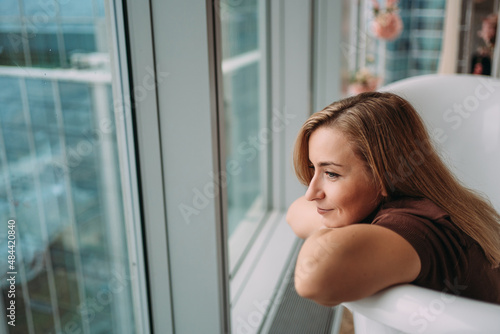 A girl at the window in an empty bathtub with a beautiful view of tall glass buildings