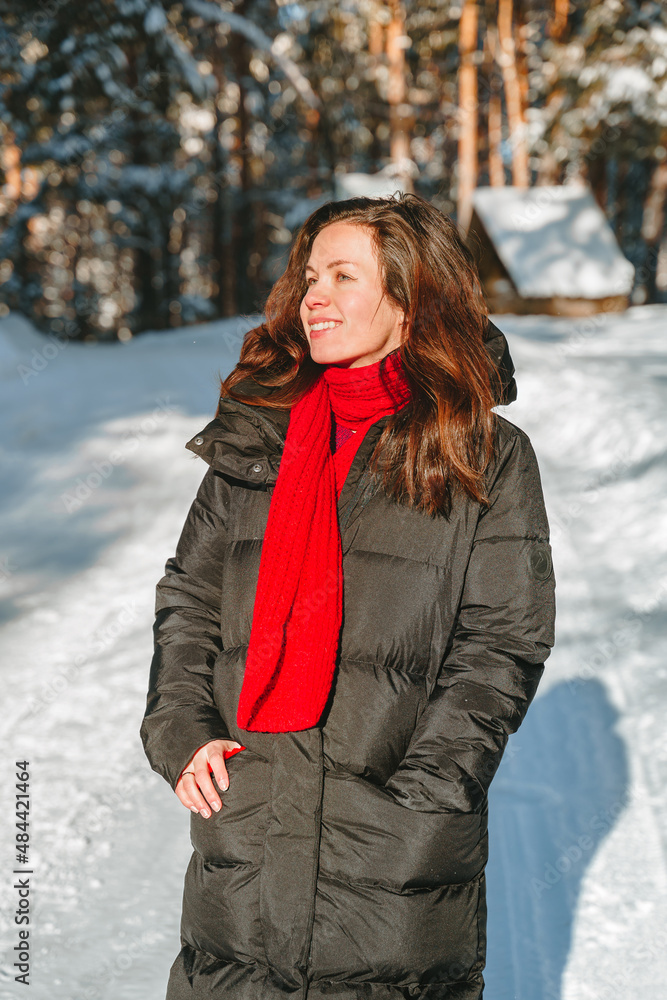 Beautiful young woman in a long down jacket in a snowy forest in winter on a sunny day Beautiful young woman in a long down jacket in a snowy forest in winter on a sunny day