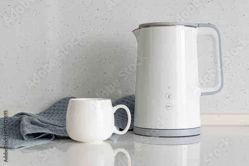 White electric kettle with a choice of heating temperature with a white porcelain mug in a bright kitchen.