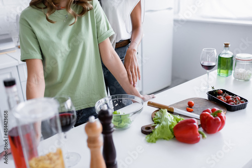 cropped view of young same sex couple standing near vegetables in kitchen.