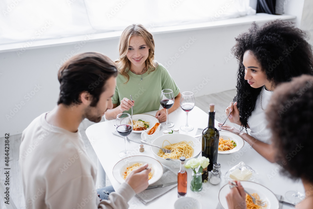 cheerful multiethnic women looking at friend near pasta on plates.