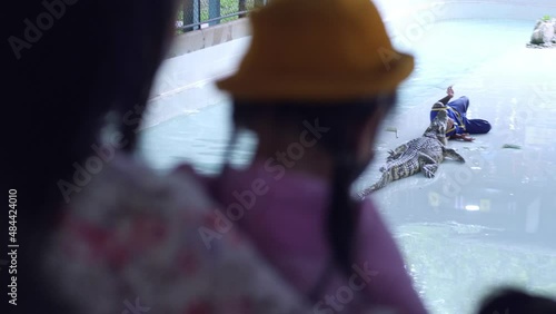 Slow motion scene of A mother holding a 5-year-old Asian girl is standing by the pond looking at the crocodile. learn things around