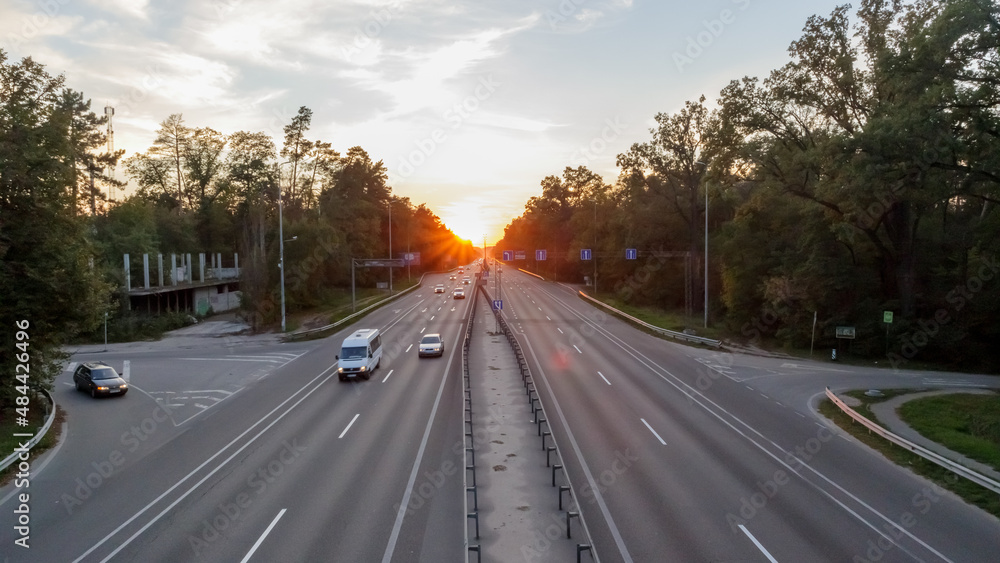 Moving cars on the motorway at sunset time. Highway traffic at sunset with cars. Busy traffic on the freeway, road top view.