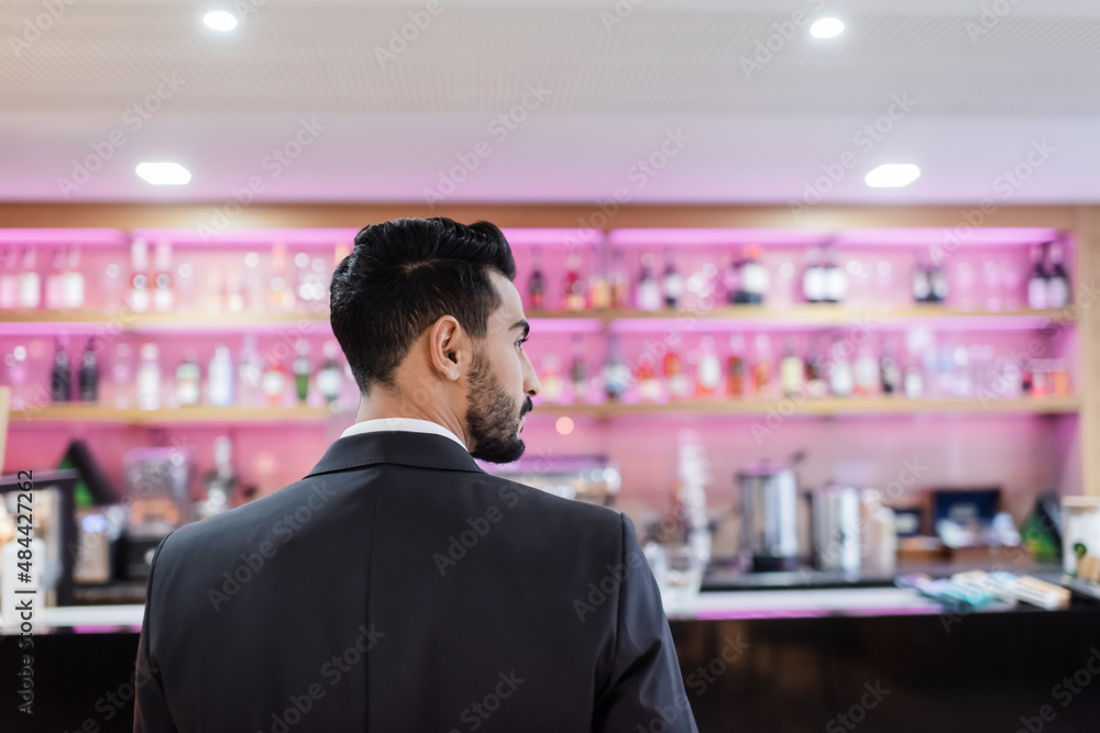 back view of bi-racial security man in black blazer near blurred lobby bar in hotel. back view of bi-racial security man in black blazer near blurred lobby bar in hotel.