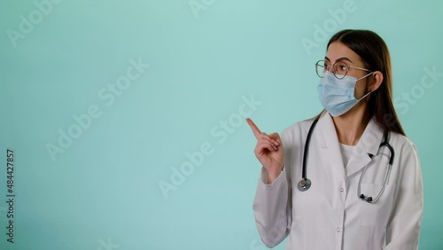 Caucasian Smiling Female Doctor In Face Mask Wear White Uniform And Stethoscope Pointing On Copyspace Isolated Over Blue Background In Studio, Place For Text Or Image, Showing Empty Space For Mock Up