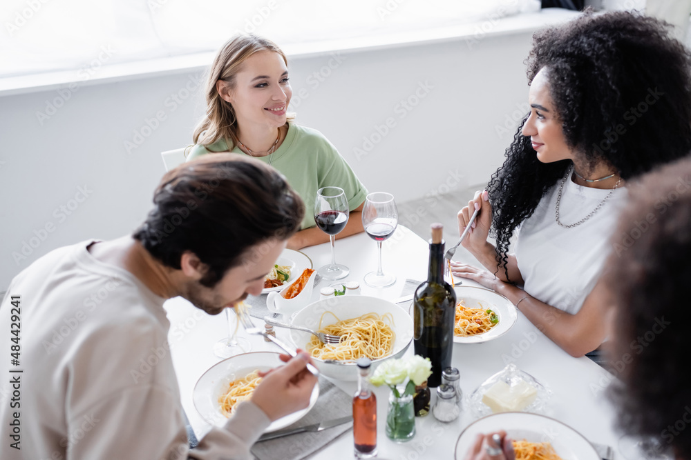 cheerful multiethnic lesbian women looking at each other near friends having lunch.