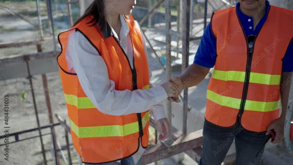 A construction worker pulls the hand of a female engineer to help lift her off the stairs at the construction site. A construction worker pulls the hand of a female engineer to help lift her off the stairs at the construction site.