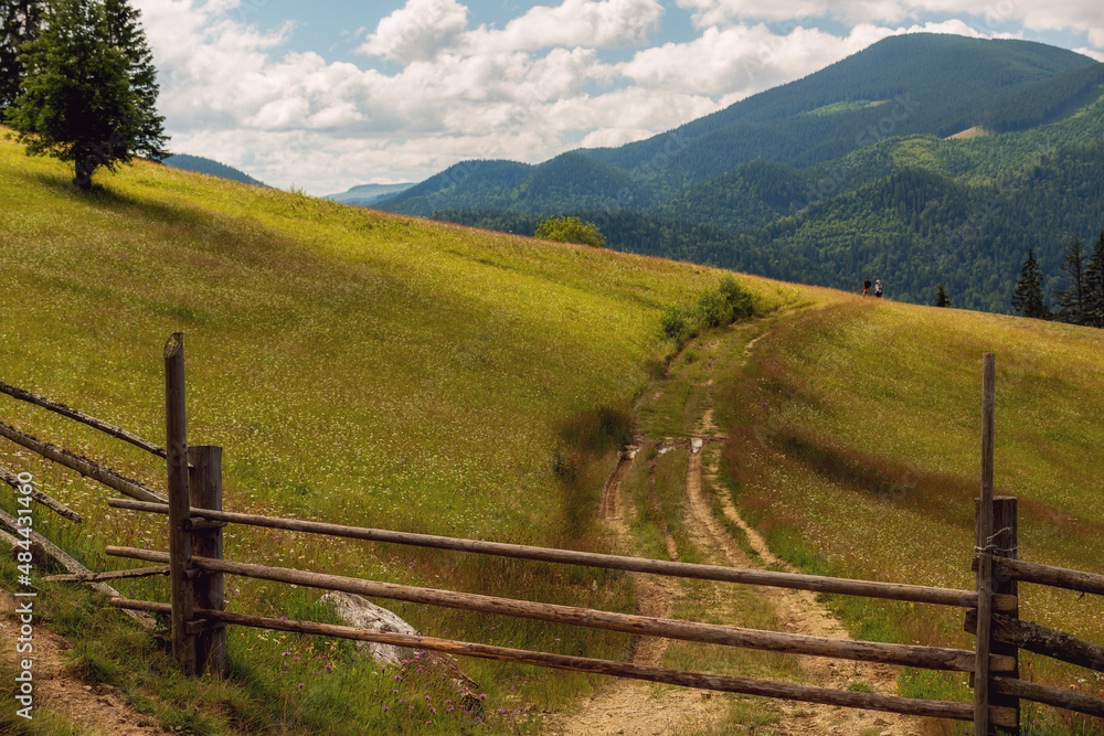 Rural mountain landscape. Dirt road among green mountains and a wooden fence.
Rural mountain landscape. Dirt road among green mountains and a wooden fence.