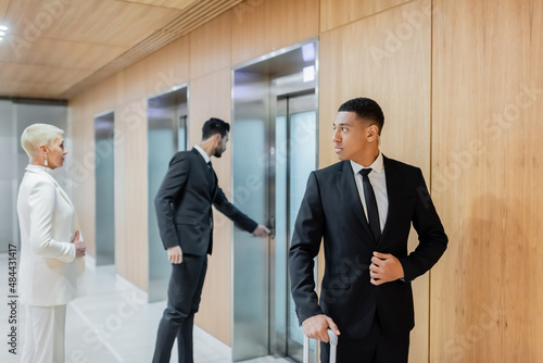 interracial bodyguards escorting senior businesswoman near elevators in hotel. photo