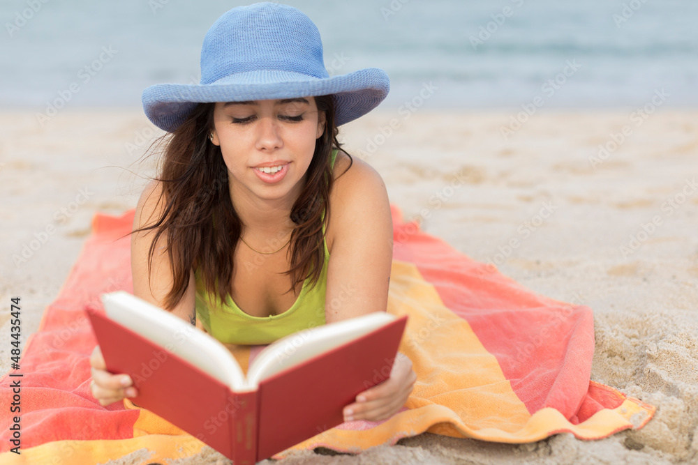 young woman at the beach on towel reading a book