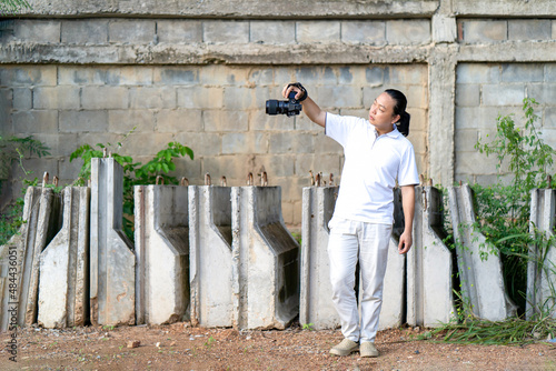 Professional Asian Chinese - Thai Camera man posture and focus in viewfinder and LED screen on mirrorless camera medium format in construction concrete area. photo