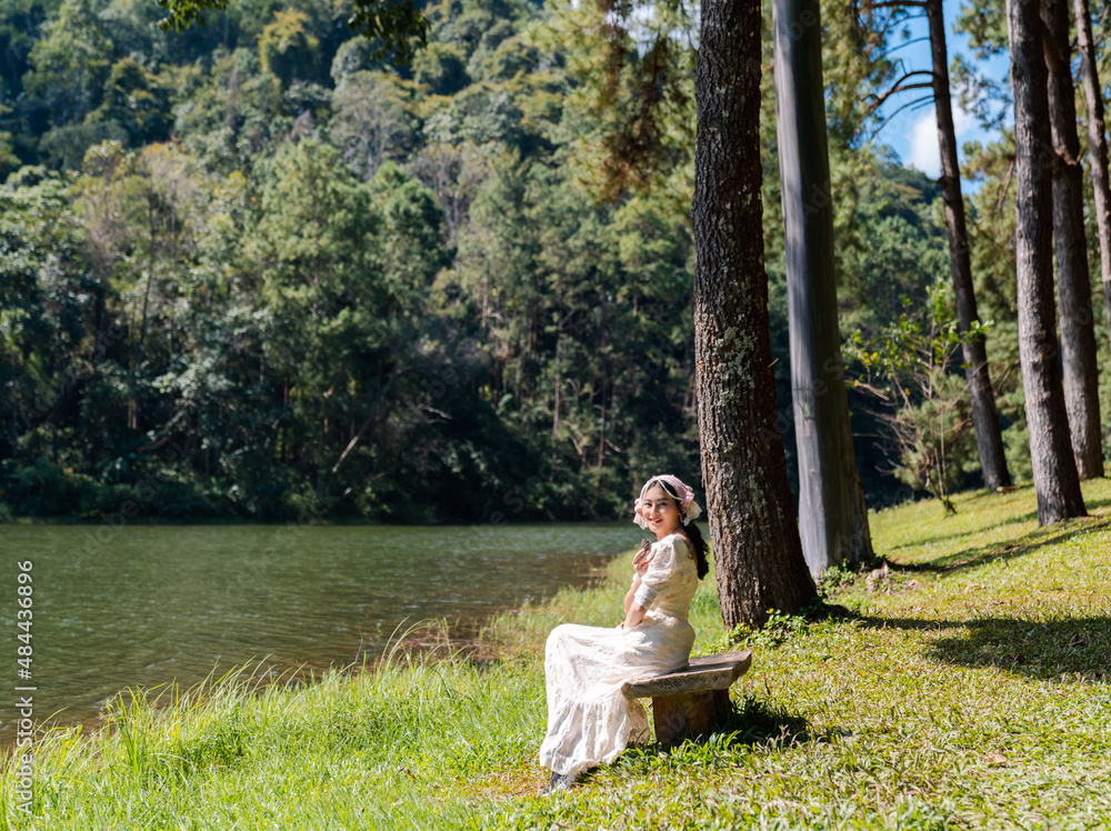 Fototapeta premium attractive Asian woman in white dress sitting in pine forest riverside at Pang Ung reservoir lake and mountain view in Mae Hong Son, Thailand