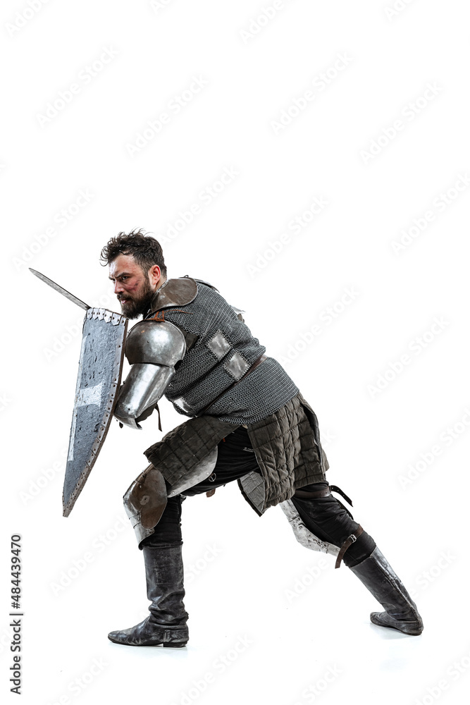 Portrait of brave medieval warrior, knight in special armor protecting himself with shield and sword isolated over white studio backgrond Portrait of brave medieval warrior, knight in special armor protecting himself with shield and sword isolated over white studio backgrond