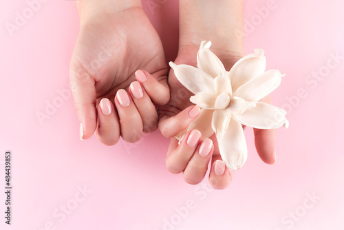Female hands with beautiful natural manicure - pink nude nails with white dried flower on pink background. Nail care concept