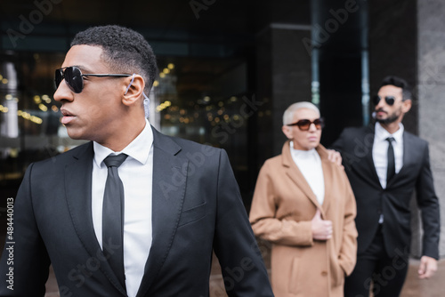 african american security man in sunglasses looking away near blurred businesswoman with bi-racial guard.