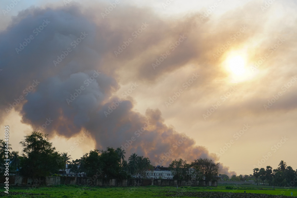 Smoke coming out of factories in the horizon, air pollution is spreading like clouds and covering the setting sun. Shot at rural village of West Bengal, India. Pollution is a global issue worldwide.