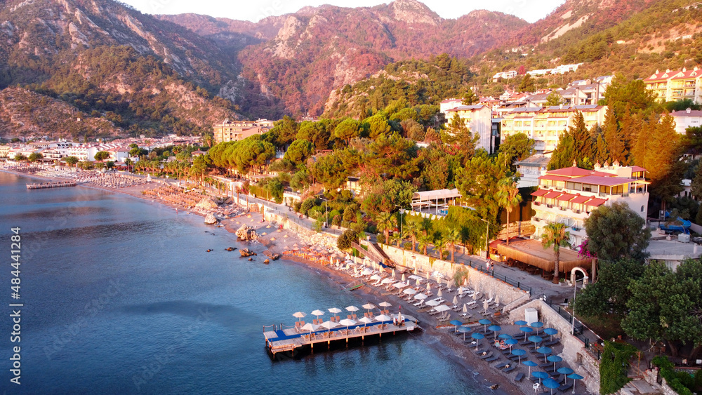 An aerial image of a beach in Turunc, Turkey. Sunrise over resort village photografed by drone. Umbrellas and sunbed in row on beach. Turunc, Turkey - September 6, 2021