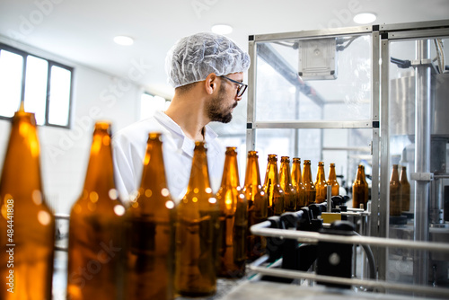 Factory worker working in alcohol beverage bottling factory. Technologist standing by production line machine and controlling beer bottles. photo