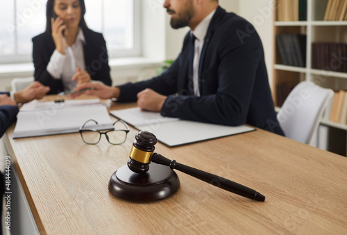Close up of judge's gavel on table, and experienced lawyer meeting with group of clients in background, talking about law and giving legal advice on property inheritance problems. Law services concept