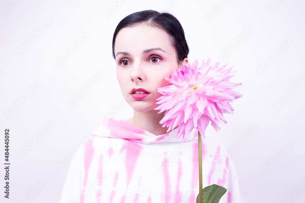 woman in a pink hoodie with pink makeup on her face holds a large flower in her hand, white background woman in a pink hoodie with pink makeup on her face holds a large flower in her hand, white background