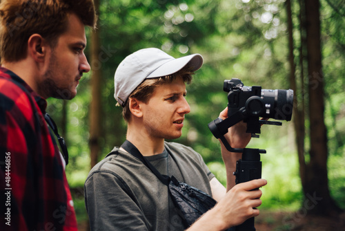 Backstage photo. Two young male video maker making video on camera with stabilizer in nature. Video content creation concept.
