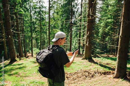 Young tourist in casual clothes and with a backpack on his back uses the Internet on a smartphone in the middle of a mountain coniferous forest.