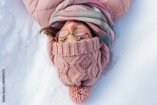 teenage girl lies on the snow in warm clothes, looking at the camera