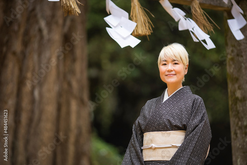 神社の境内に立つ着物姿（大島紬）の金髪日本人女性
