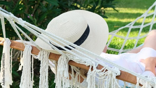 female in a straw hat is resting in a hammock around the palm trees and enjoying the tranquility and relaxation. Vacation concept