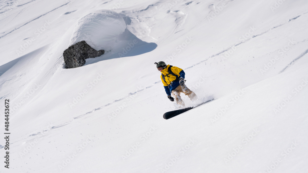 Freerider snowboarder running down the picturesque alpine landscape. Fresh powder snow, blue sky on background. 