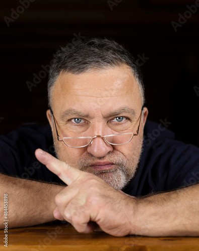 An adult man who looks like his father looks over the top of his reading glasses and shakes his finger disapprovingly about what someone has done or is going to do.