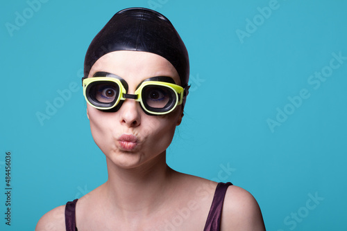 woman swimmer, in a swimming cap, glasses and a swimsuit, blue background