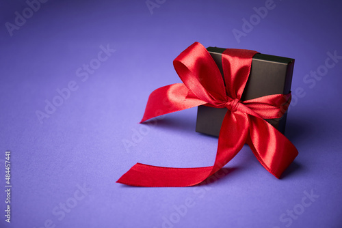 black gift with red ribbon on purple background. Valentine's day. Birthday or Holidays concept. Copy space