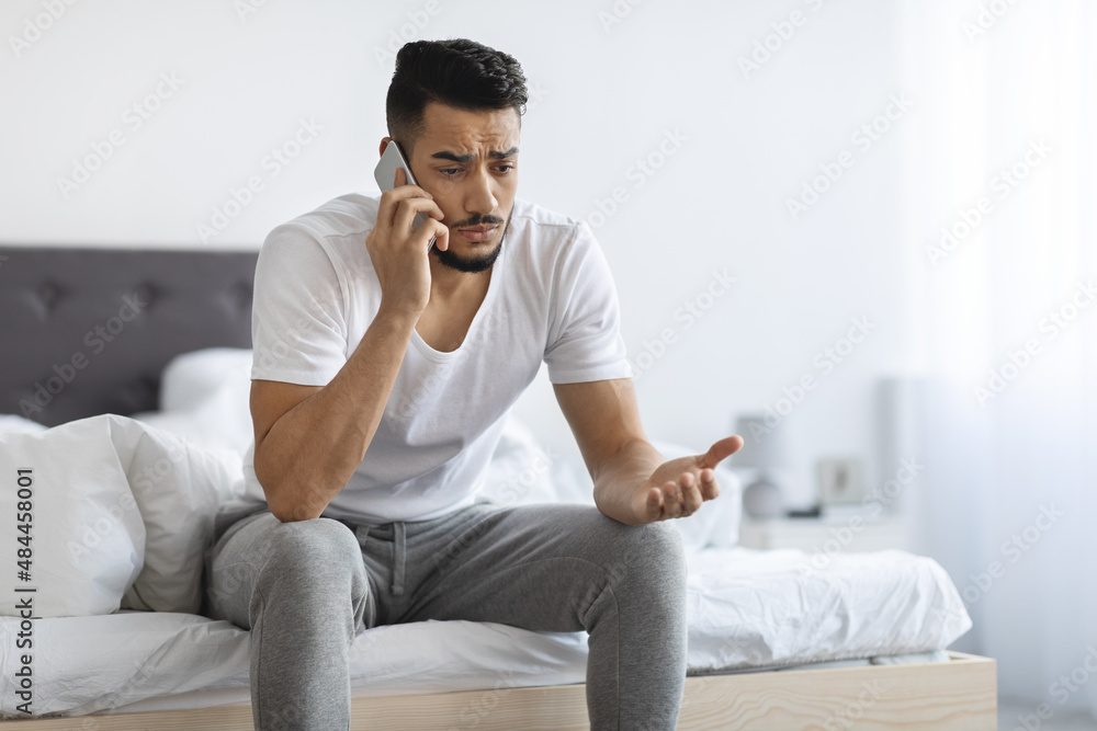 Portrait Of Worried Young Arab Man Talking On Cellphone In Bedroom Portrait Of Worried Young Arab Man Talking On Cellphone In Bedroom