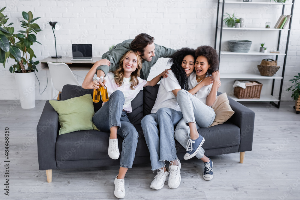 happy man holding bottles of beer and hugging interracial women on sofa. happy man holding bottles of beer and hugging interracial women on sofa.