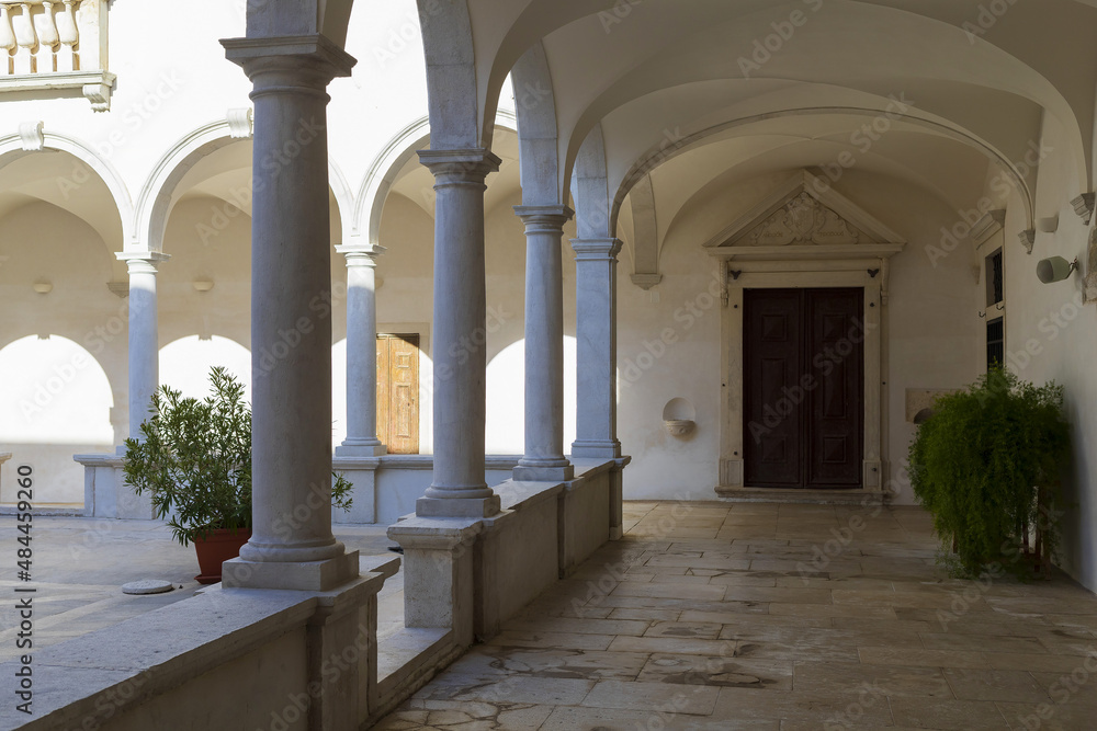 Inner courtyard of white baroque building with colonnade and dark wooden door on sunny day