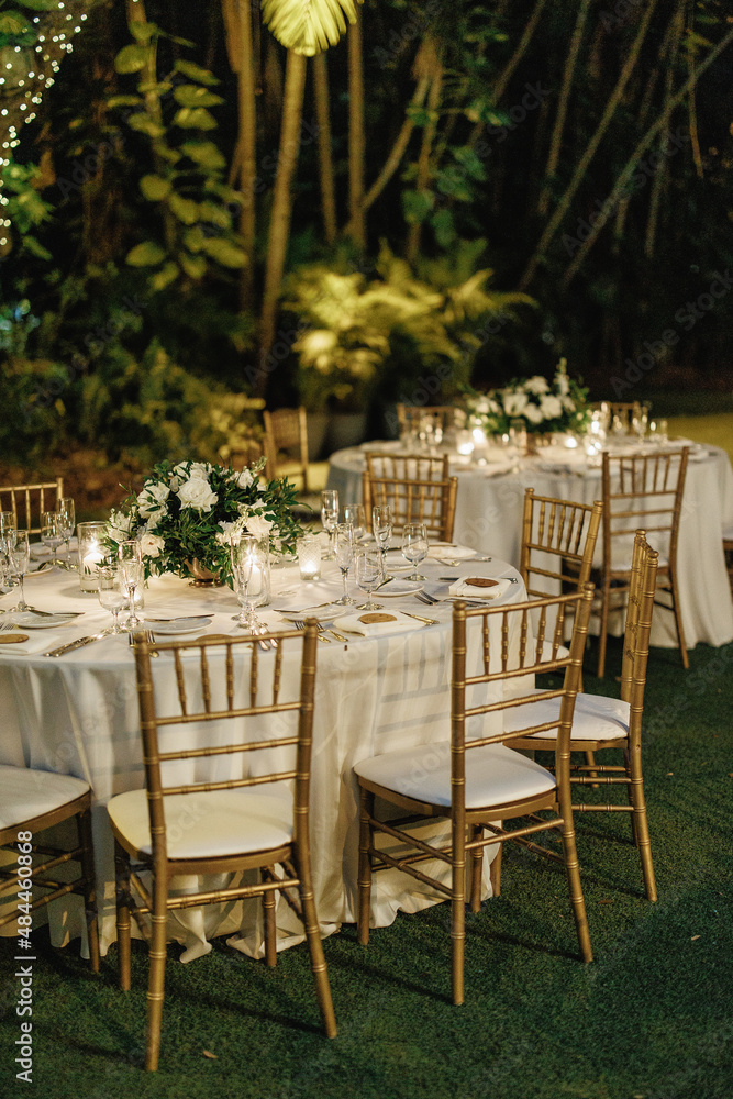 Wedding table setting decorated with bouquets of white roses Served table for dinner on the wedding party at the hotel restaurant Table set up for a special event with roses and greenery outdoors