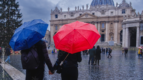 Young couple under umbrellas standing near St Peter's basilica at Vatican. Holidays for couple in Italy