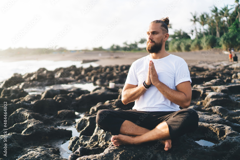 Harmony and meditation training during morning yoga at coastline with rocks, Caucaisan male in sportswear sitting in lotus pose during hatha practice for exercising body concentration in asana Harmony and meditation training during morning yoga at coastline with rocks, Caucaisan male in sportswear sitting in lotus pose during hatha practice for exercising body concentration in asana