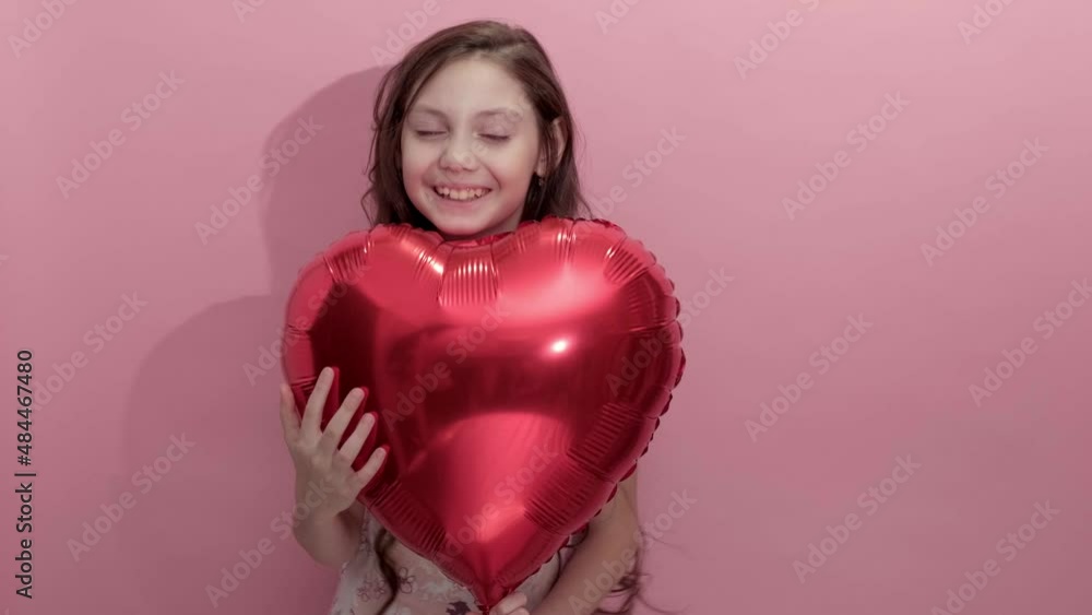 4K. Beautiful girl on a pink background with a red balloon in the shape of a heart. Happy little caucasian girl with red balloon. valentines day or mothers day concept. Congratulations on day love 4K. Beautiful girl on a pink background with a red balloon in the shape of a heart. Happy little caucasian girl with red balloon. valentines day or mothers day concept. Congratulations on day love