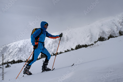 Ski tourer dressed in professional clothes is steping on skis during winter hiking.